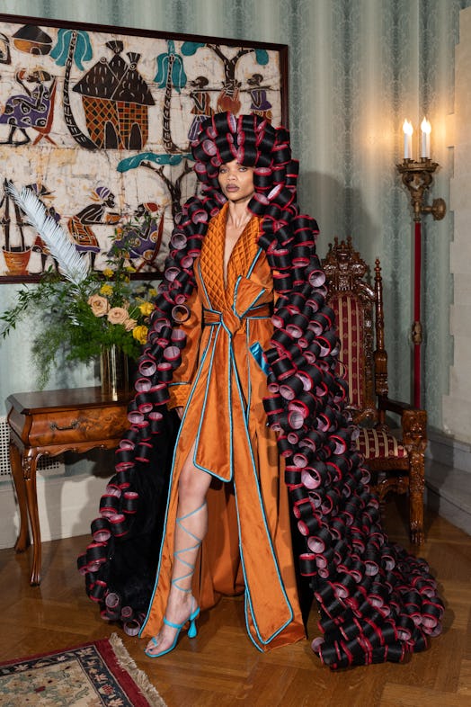 A model in Pyer Moss's orange silk robe, light blue strappy sandals and hair rollers that go till th...