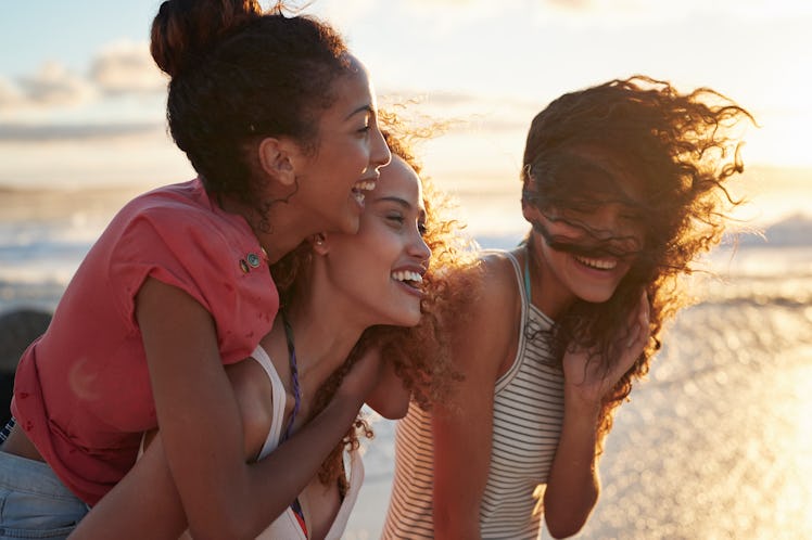 3 young women looking out at the water at the beach, with their salty hair blowing in the wind, watc...