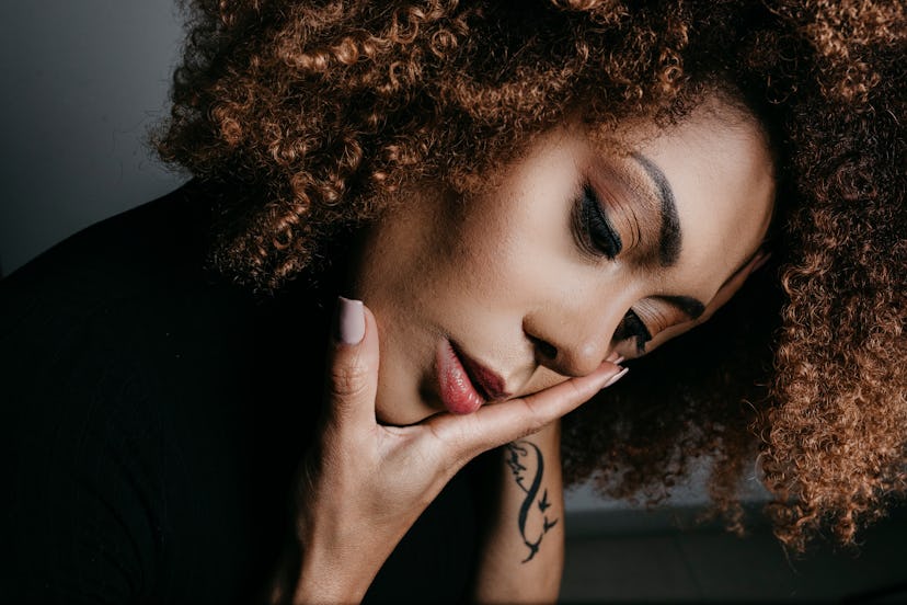 Woman holding her face, with tattoo on her arm