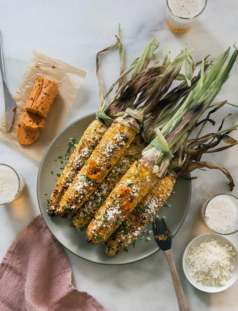 overhead view of corn on the cob, husks on, with chipotle bourbon butter and cheese,