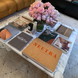 A coffee table, a vase of pink roses and various coffee table books taking up the whole table