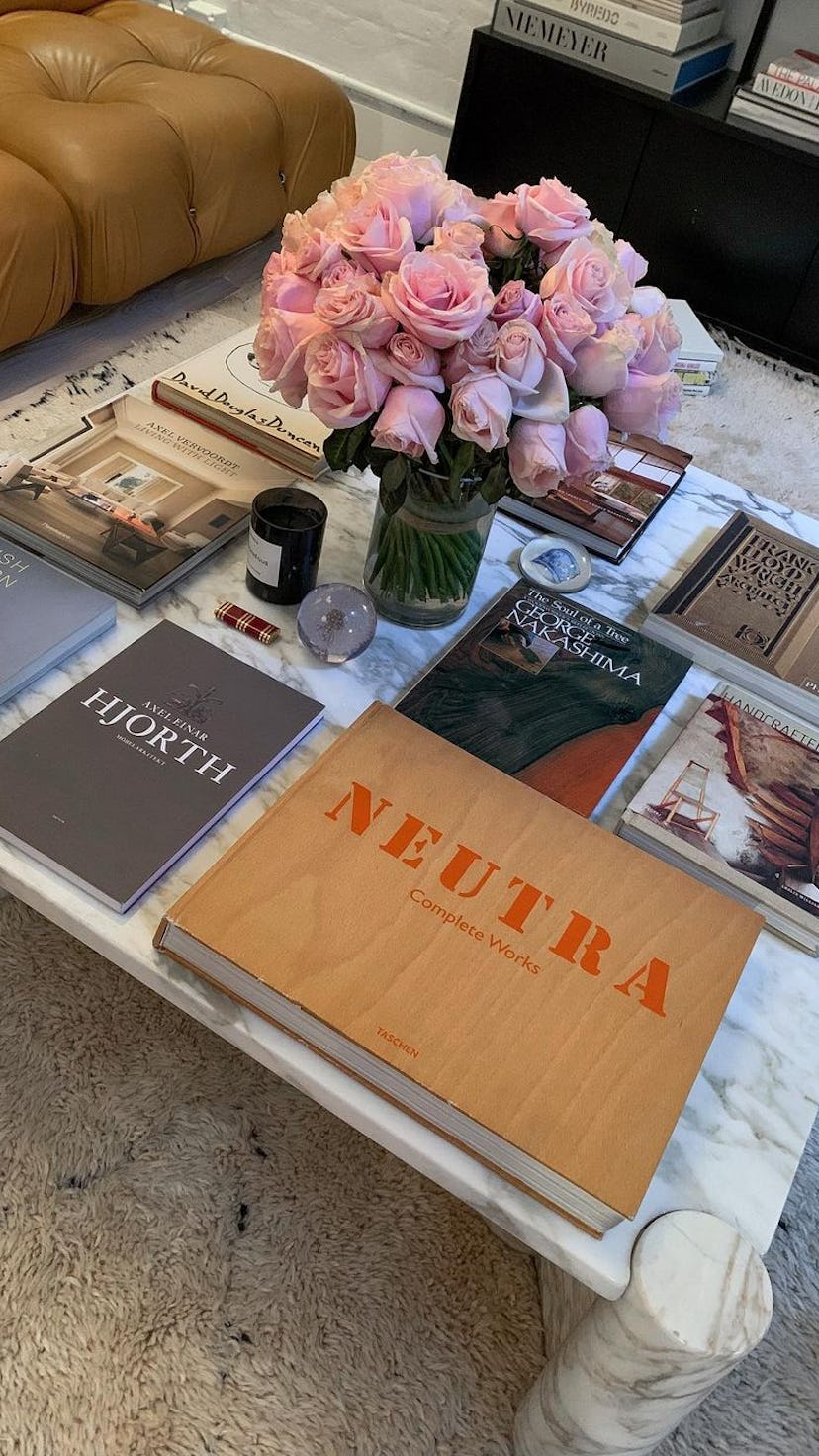 A coffee table, a vase of pink roses and various coffee table books taking up the whole table