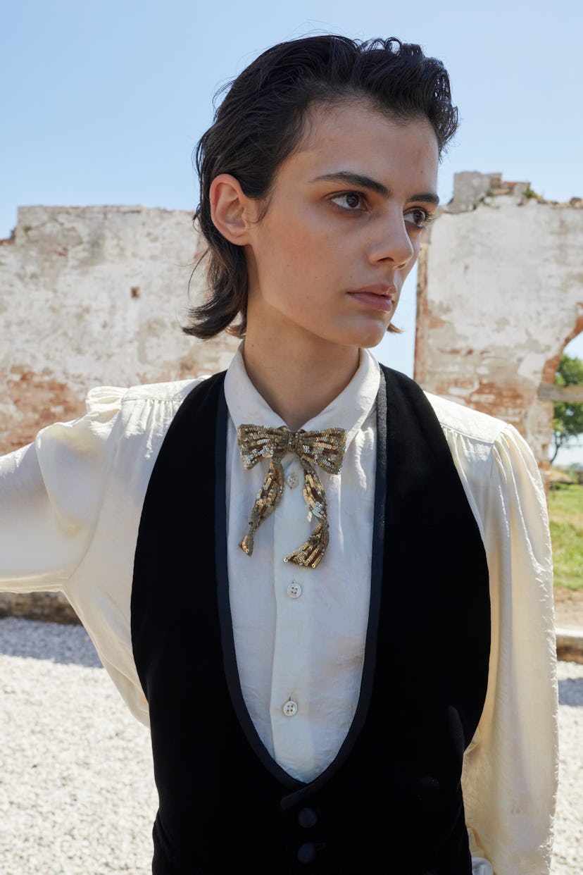 A model posing in a white shirt, a black waistcoat and a gold sequin bowie at Men’s Fashion Week Spr...