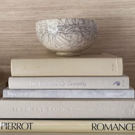 Four coffee table art books stacked on top of each other with a bowl on the top of them