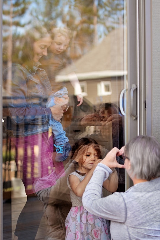 A grandmother and granddaughter pointing heart signs with their hands at opposite sides of a window