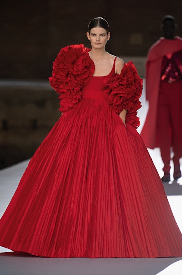 A model walking the runway in a red Valentino gown with flowers made of the same material on the top...