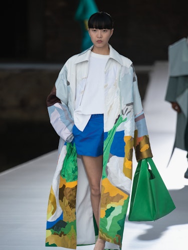 A model in a white illustrated coat, a white shirt and blue shorts at the Valentino Couture Fall 202...
