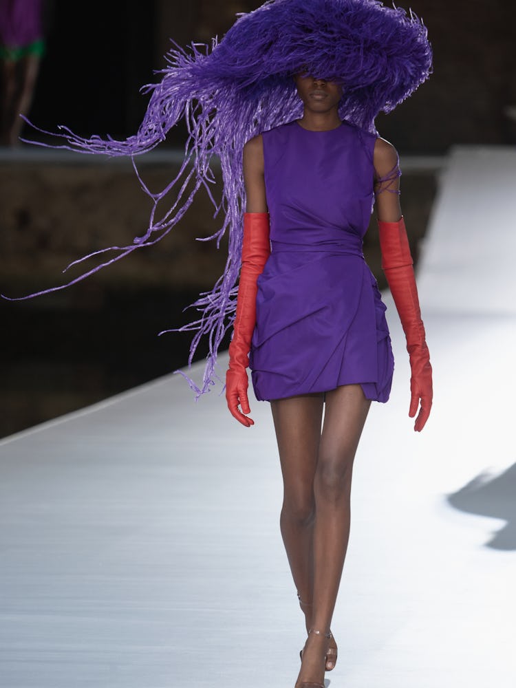 A model in a purple dress and hat and red gloves at the Valentino Couture Fall 2021 Couture