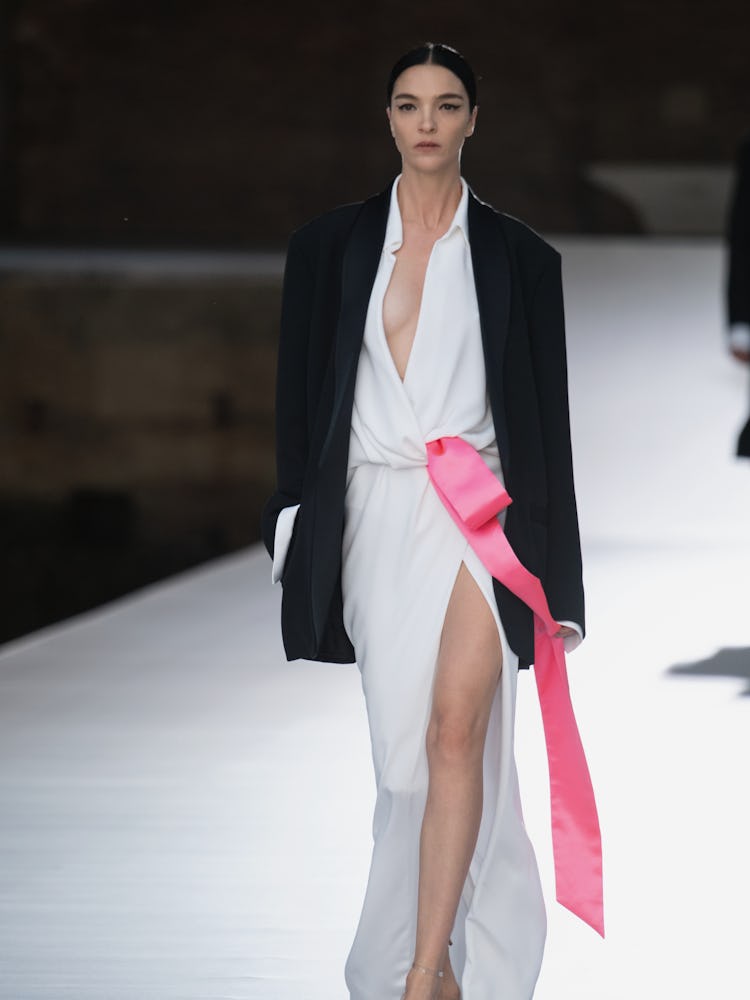 A model in a white dress with a pink bow and a black blazer at the Valentino Couture Fall 2021 Coutu...