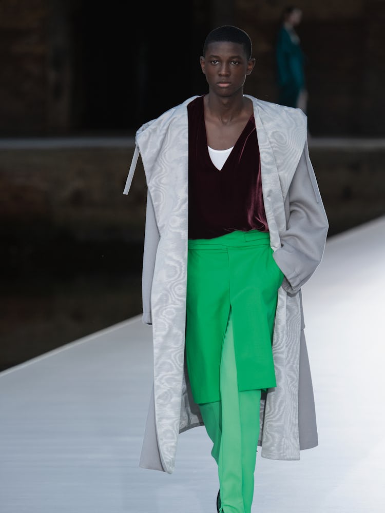 A model in a beige coat, green skirt-dress and brown top at the Valentino Couture Fall 2021 Couture