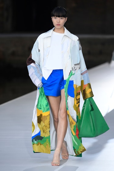 A model in a white illustrated coat, white shirt and blue shorts at the Valentino Couture Fall 2021 ...