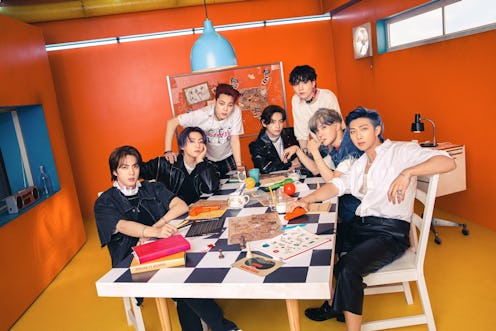 BTS poses together at a table filled with books and cups of tea.