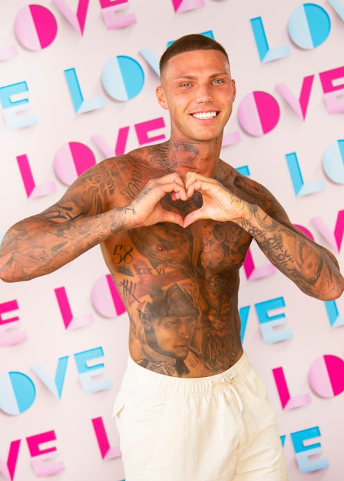 Love Island contestant Danny pictured in cream coloured swimming trunks, smiling and making a heart ...