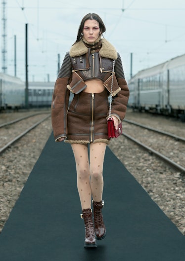 A female model walking while wearing a brown zip-away half leather jacket and a brown zip-away skirt
