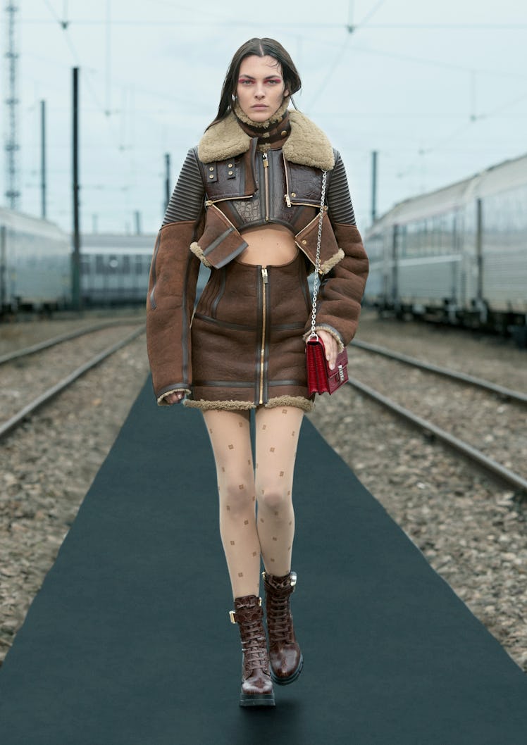 A female model walking while wearing a brown zip-away half leather jacket and a brown zip-away skirt