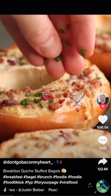 A man sprinkles chives onto a quiche-stuffed bagel from a TikTok recipe. 