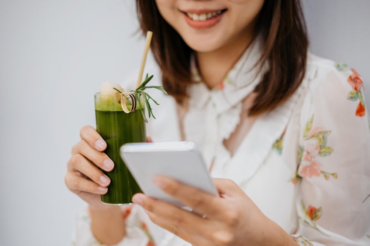 Young woman holding a cup of matcha green tea before posting a pic on Instagram with matcha puns, ma...