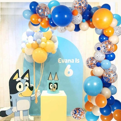 Birthday party backdrop with "Bluey" character, cake, and balloon arch