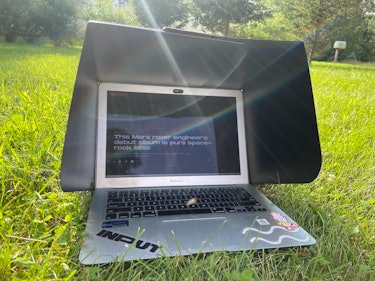 A Macbook Air with a black sunshade over it sits in the grass on a sunny day