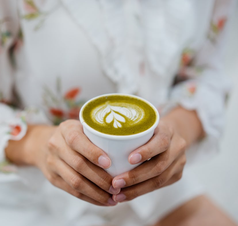 Young woman holding a cup of matcha, thinking of matcha puns, quotes, and captions to post on Instag...