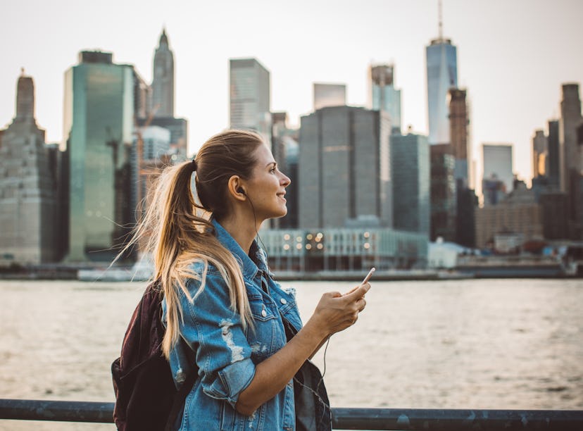 Young woman smiling with the NYC skyline in the background before posting a pic on Instagram with sk...