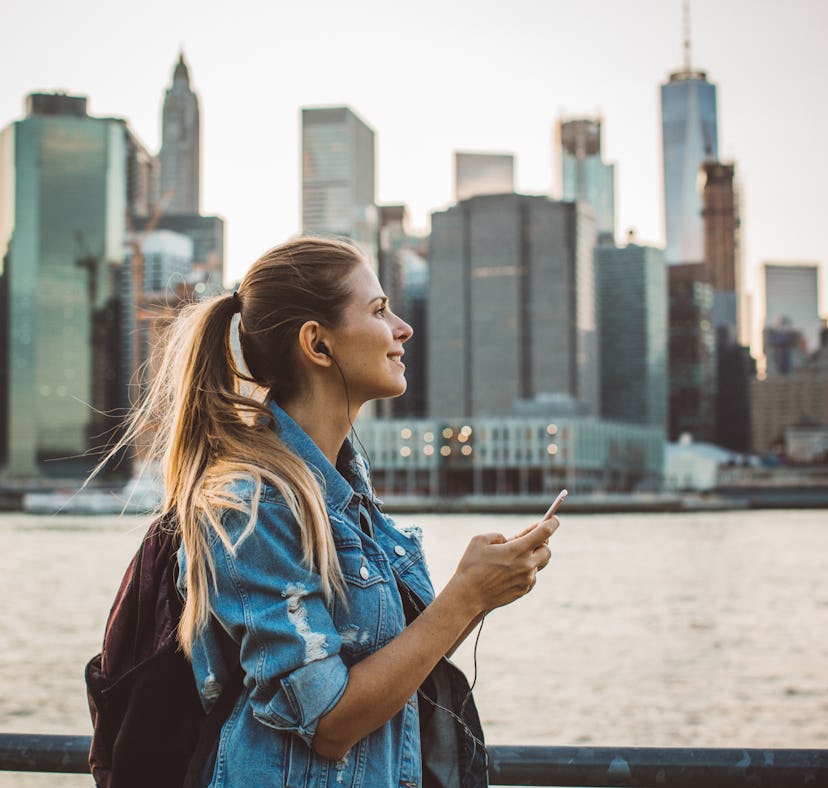 Young woman smiling with the NYC skyline in the background before posting a pic on Instagram with sk...