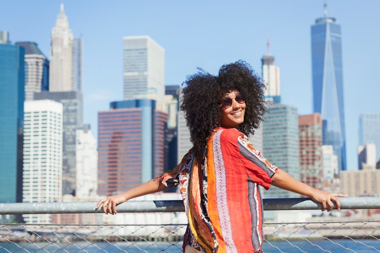 Young woman smiling with the NYC skyline in the background before posting a pic on Instagram with sk...