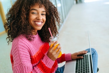Young woman wearing an oversized sweater with a laptop and juice.