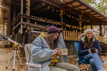 2 young friends drinking hot chocolate at a cabin in the fall before posting a pic on Instagram with...