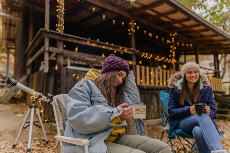 2 young friends drinking hot chocolate at a cabin in the fall before posting a pic on Instagram with...