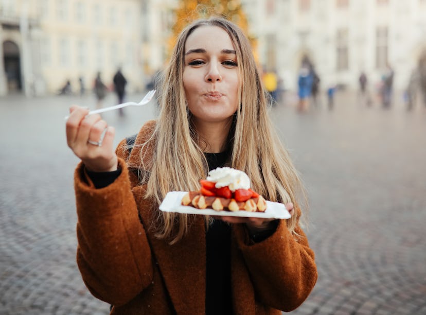 Young woman eating Belgian waffles outside before posting a foodie pic on Instagram with waffle quot...