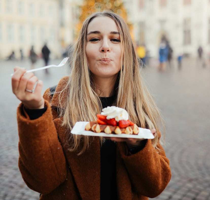 Young woman eating Belgian waffles outside before posting a foodie pic on Instagram with waffle quot...
