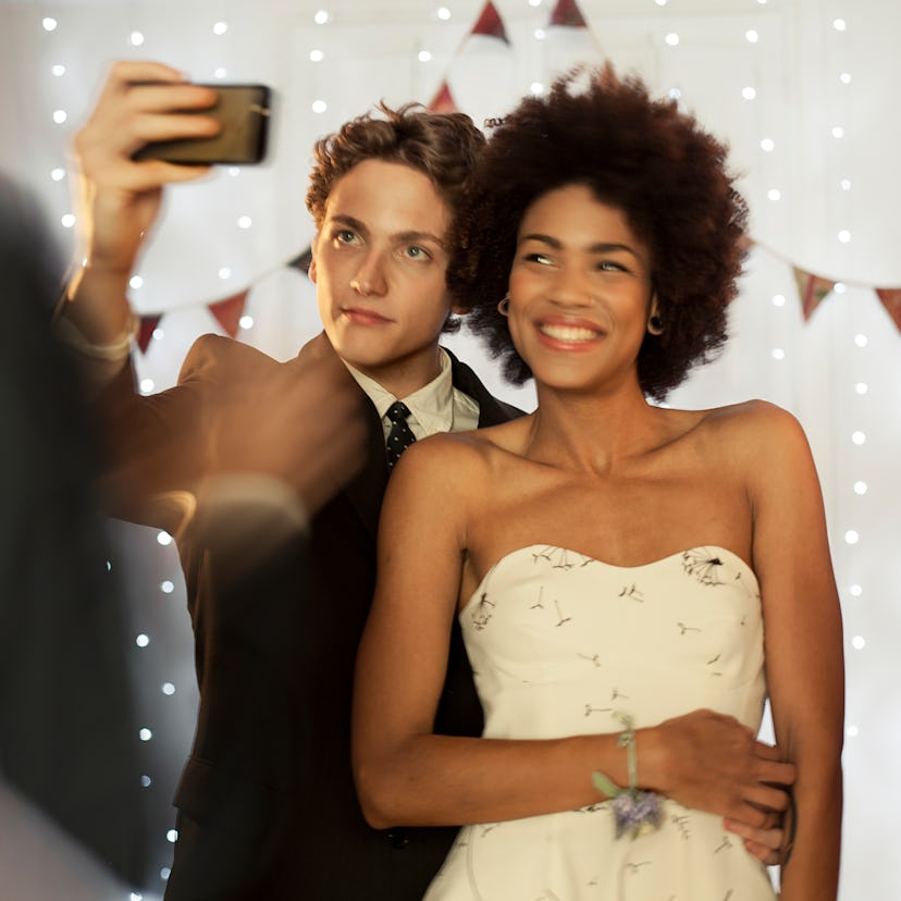 A young prom king and queen posing for a selfie before posting Instagram captions.