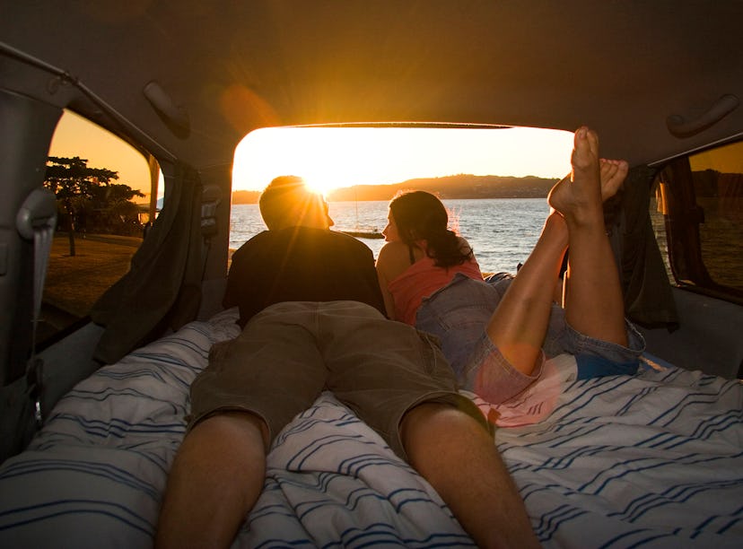 Couple watching sunset from bed inside campervan before posting on Instagram with romantic sunset qu...