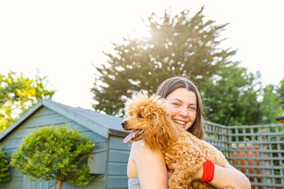 Happy young woman holding her dog, taking a pic to post with dog point of view Instagram captions.