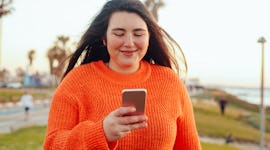 Young woman wearing an orange oversized sweater, looking at her phone trying to figure out which swe...