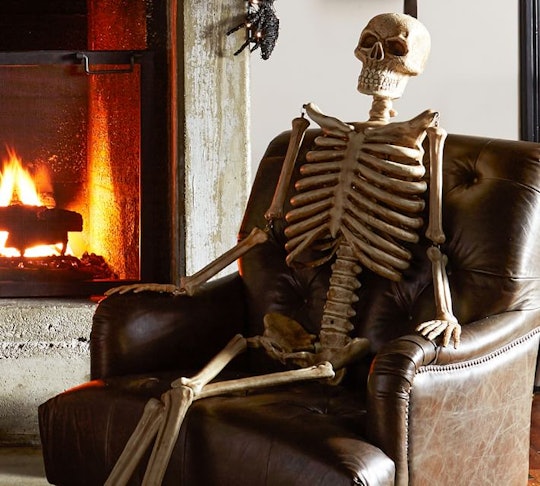 fake halloween skeleton from pottery barn sitting on chair indoors by fireplace