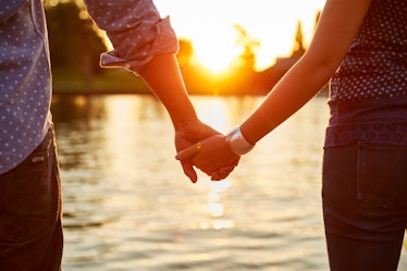 Young couple holding hands with each other at sunset before posting a pic on Instagram with romantic...