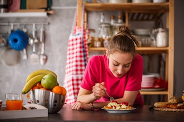 Young woman eating breakfast in her kitchen before posting a foodie pic on Instagram with waffle pun...