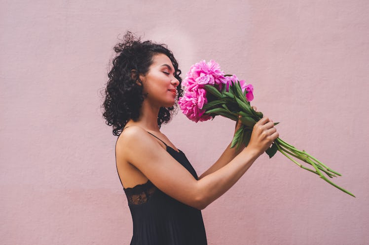 Young woman smelling a bouquet of flowers before posting a pic on Instagram with flower quotes and c...