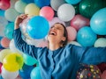 Happy young woman in front of a balloon wall, celebrating her birthday alone.