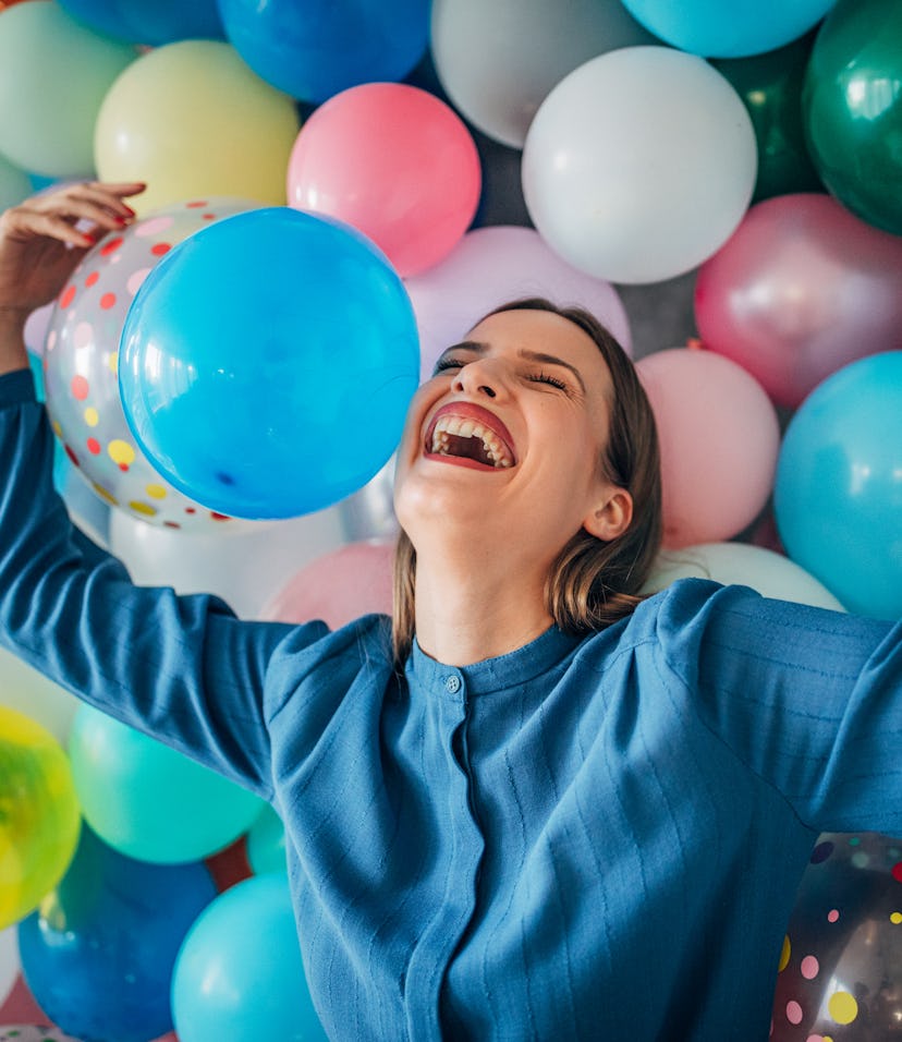Happy young woman in front of a balloon wall, celebrating her birthday alone.