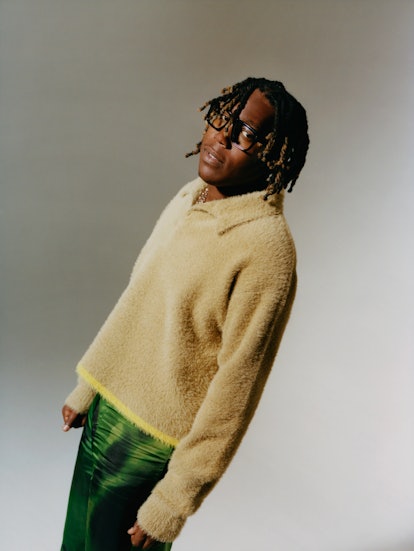 Don Toliver leaning backward, wearing glasses and a light brown fleece shirt with green pants