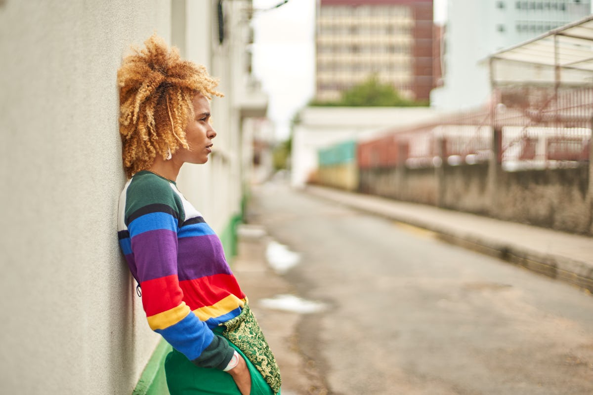 Young woman in a rainbow sweater leaning against a wall, showing her most secret fear, per her zodiac sign.