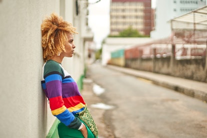 Young woman in a rainbow sweater leaning against a wall, showing her most secret fear, per her zodia...