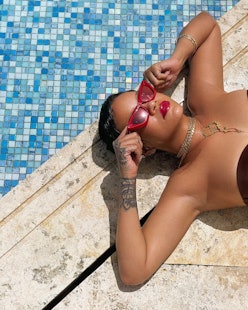 Rihanna in red sunglasses wearing Fenty Beauty Gloss Bomb