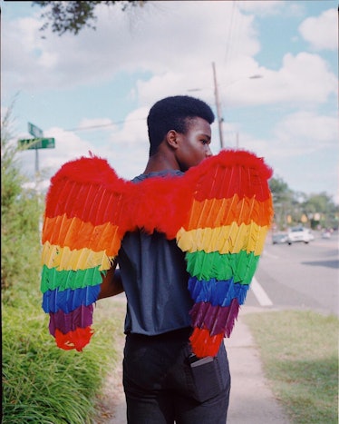 Photograph by Kennedi Carter of a person with wings in rainbow colors walking down a street