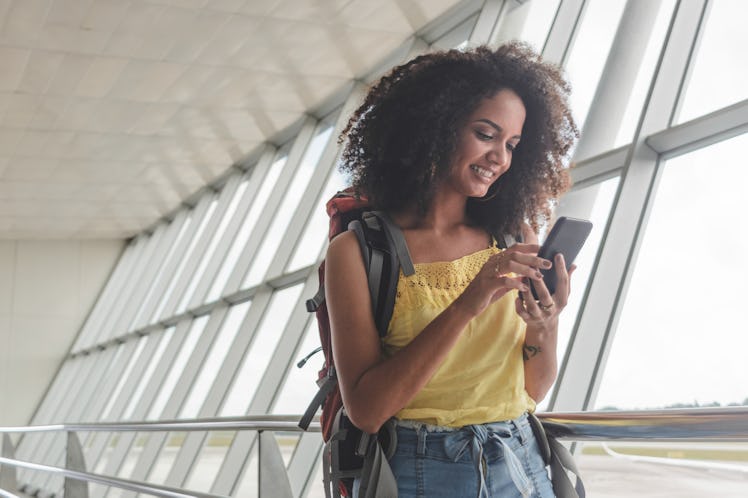 Young traveler with a travel bio on her Instagram, looking at her phone in the airport.