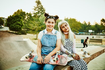 2 smiling friends sitting on ramp in a skate park, taking a pic before posting funny birthday captio...