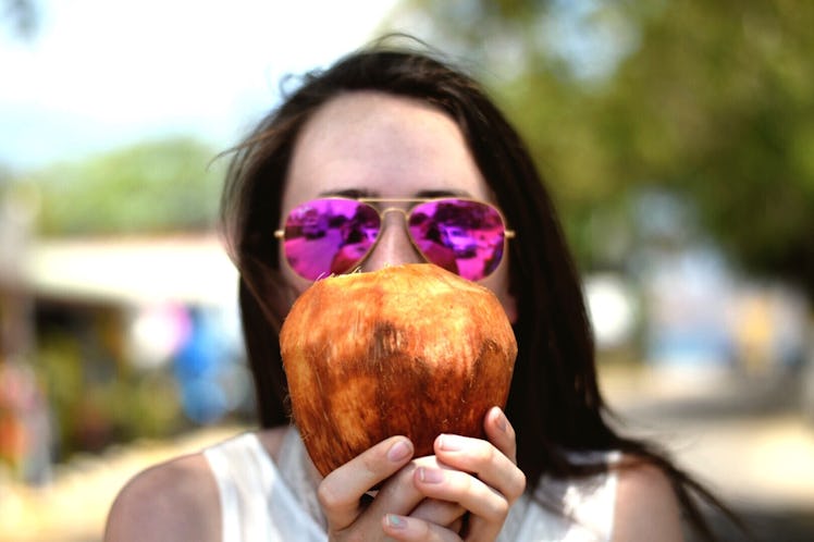 Young woman with pink sunglasses, holding a coconut before posting on Instagram with coconut puns, c...